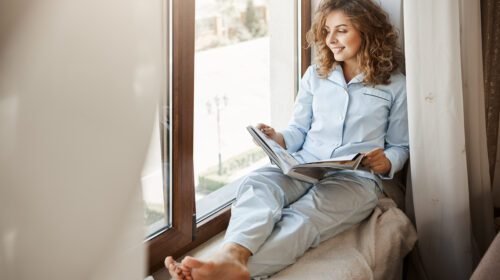 charming businesswoman having relaxing time home pleased good looking adult woman nightwear sitting window sill gazing street holding fashion magazine reading about lifestyle
