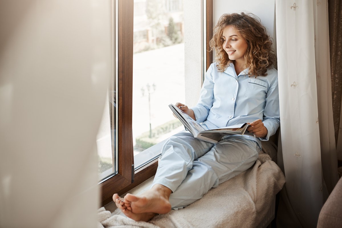 charming businesswoman having relaxing time home pleased good looking adult woman nightwear sitting window sill gazing street holding fashion magazine reading about lifestyle